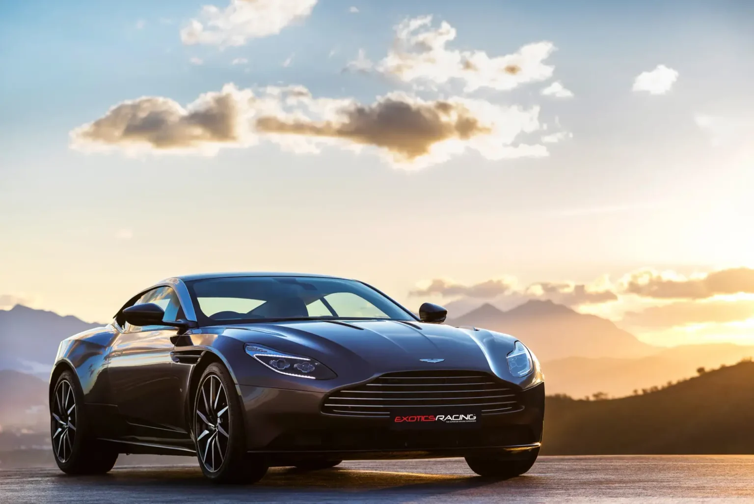 Black Aston Martin DB11 parked in front of a mountain range at sunset