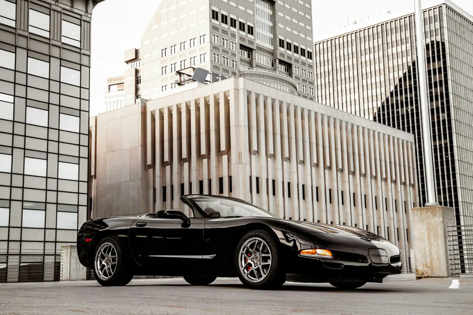 Black Chevrolet Corvette C4 convertible parked on a rooftop with modern city buildings in the background